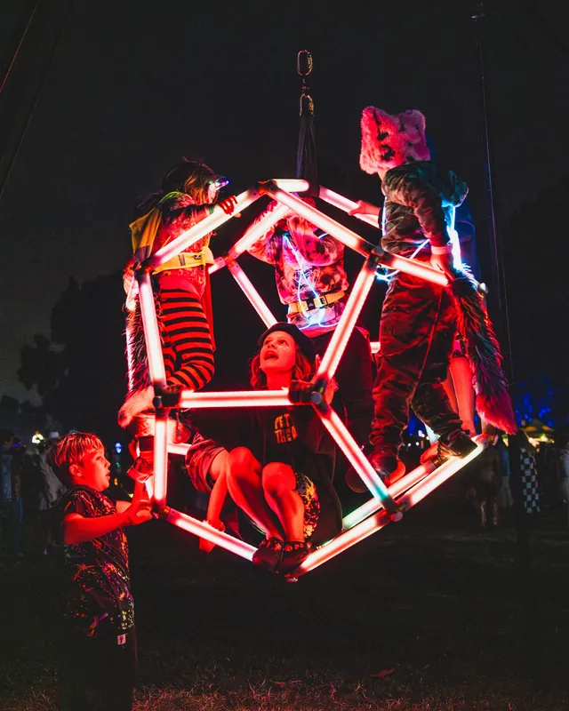 Children and adults climbing on the red-lit dodecahedron at a festival