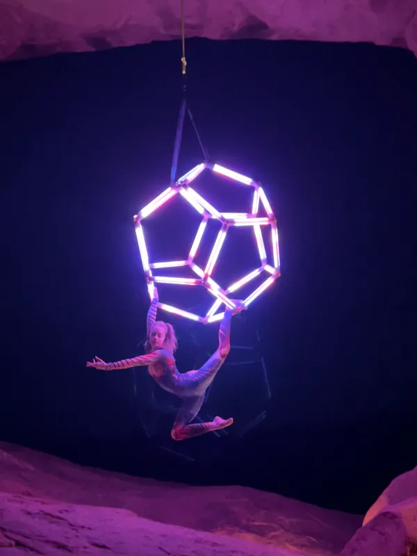 Performer suspended from a glowing purple LED dodecahedron