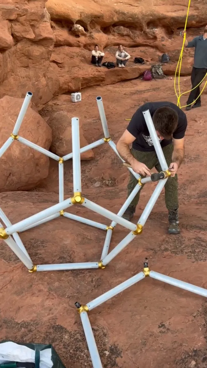 Dodecahedron frame being assembled on red rock terrain, showing steel tubes and gold-colored investment-cast connectors