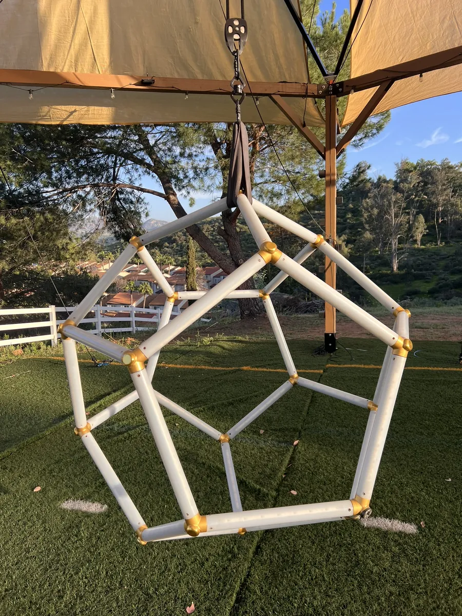 Assembled dodecahedron hanging from a canopy structure on a green lawn